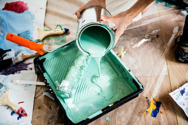 Man standing off-screen while pouring pastel green paint into a pain tray