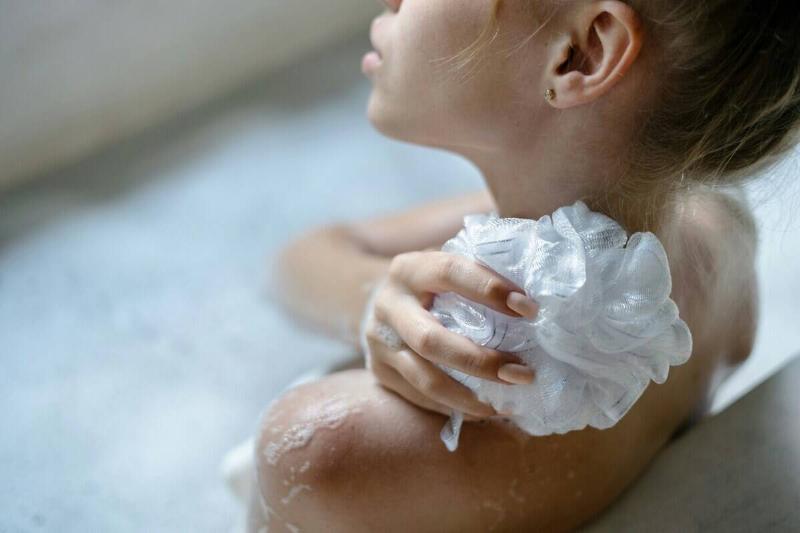 Woman using a loofa on her shoulder while sitting in a bath