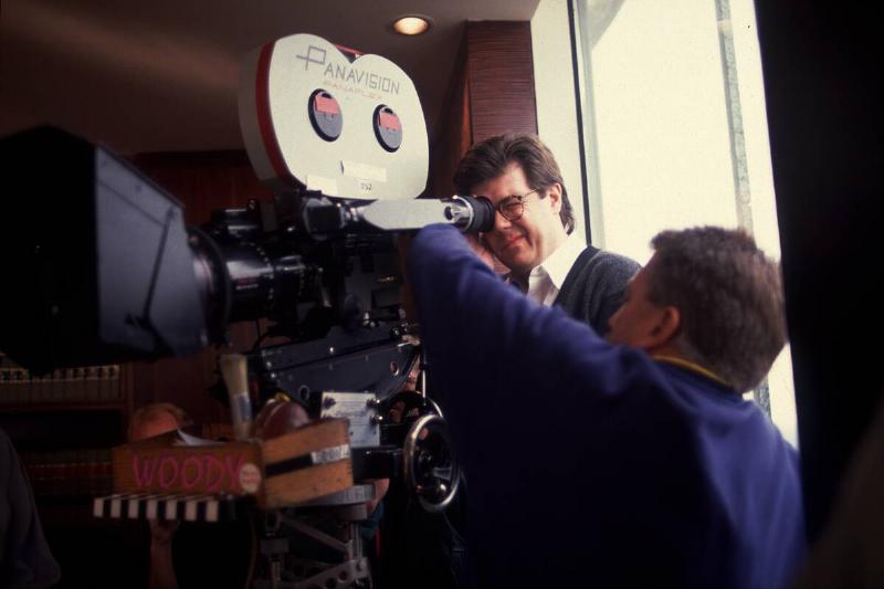 John Hughes standing behind a camera on a film set. A man is standing beside him