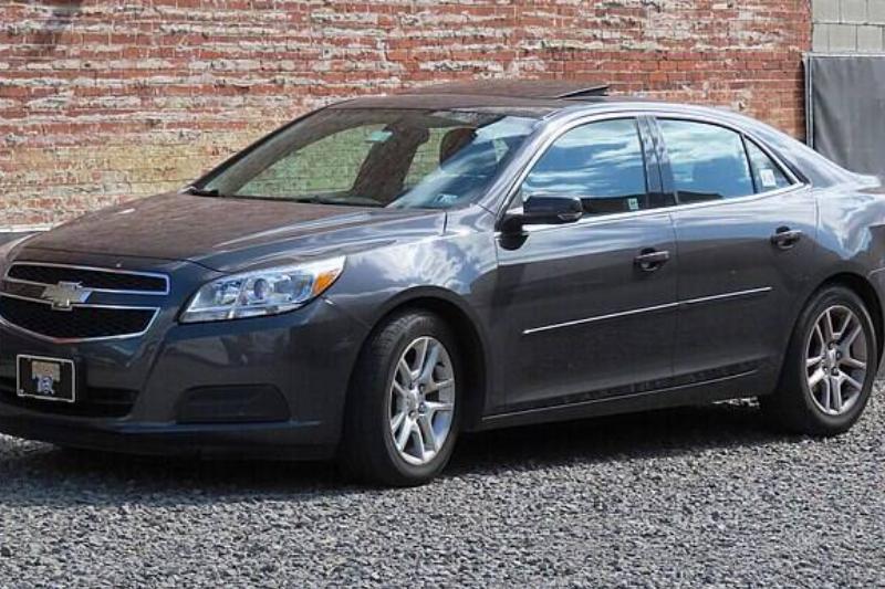 Dark grey 2013 Chevrolet Malibu parked next to a brick building
