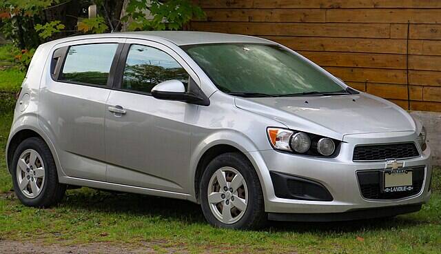 Silver 2014 Chevrolet Sonic parked next to a wooden fence