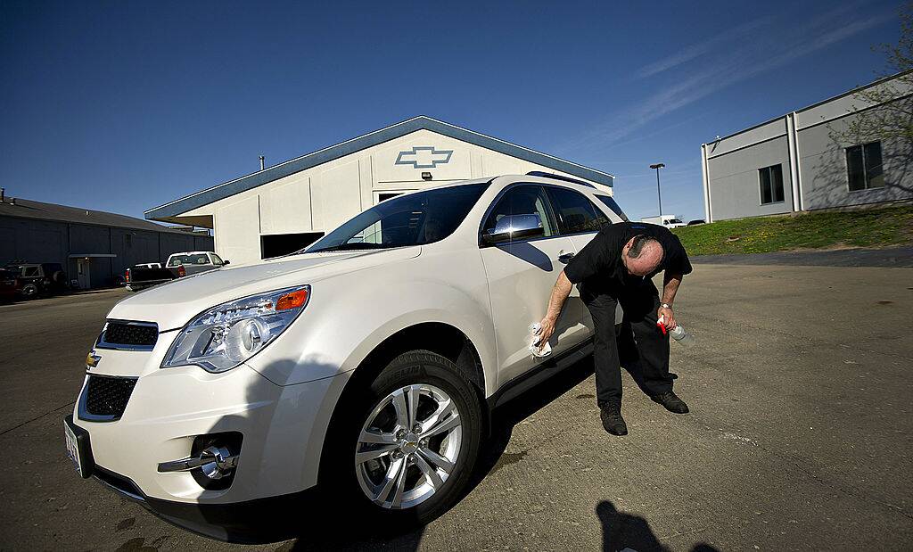 Man wiping the driver's-side door of a white 2013 Chevrolet Equinox