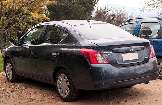 Black 2016 Nissan Versa parked in a gravel parking lot, next to a blue vehicle
