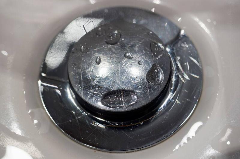 Close-up of a metal drain and stopper in a ceramic sink