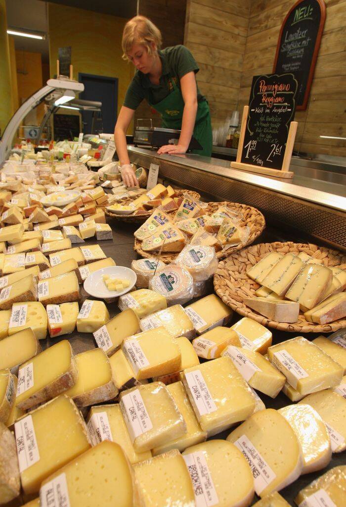 Woman standing over a store fridge filled with cheese