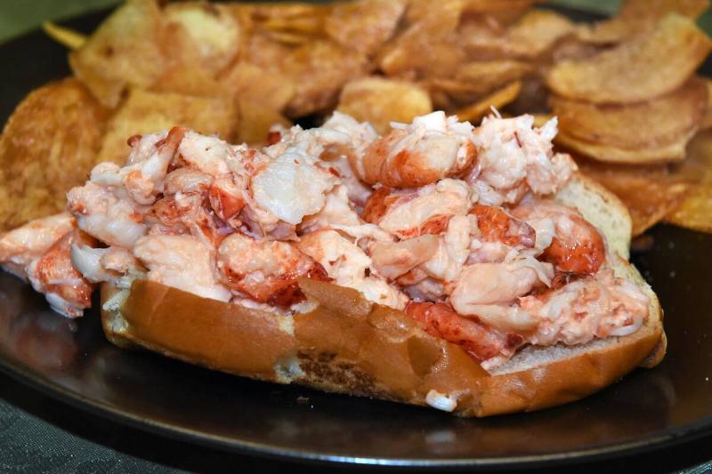 Lobster roll next to potato chips on a plate