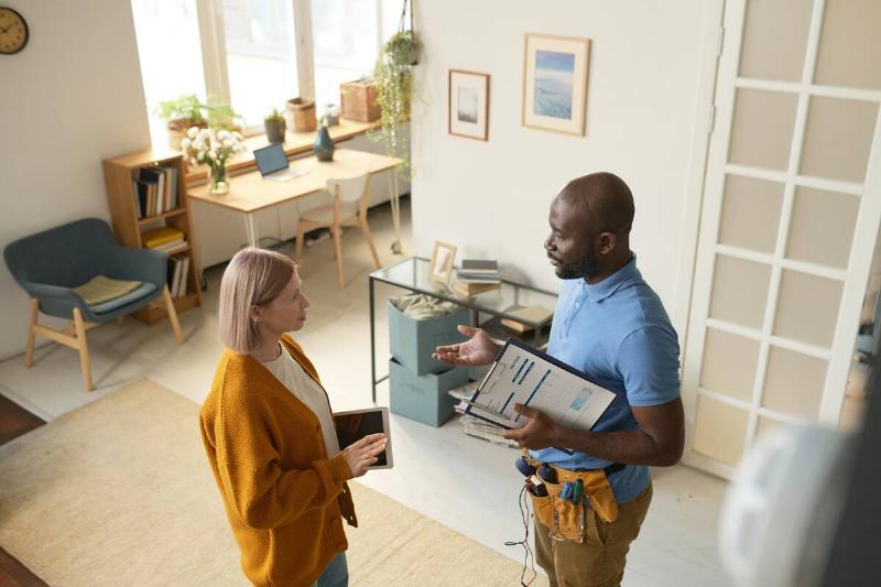 Overhead view of a construction worker speaking to a woman in the middle of a living room