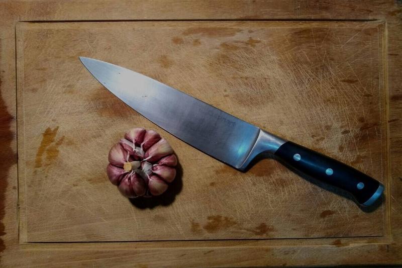 Knife next to a garlic bulb on a wooden cutting board