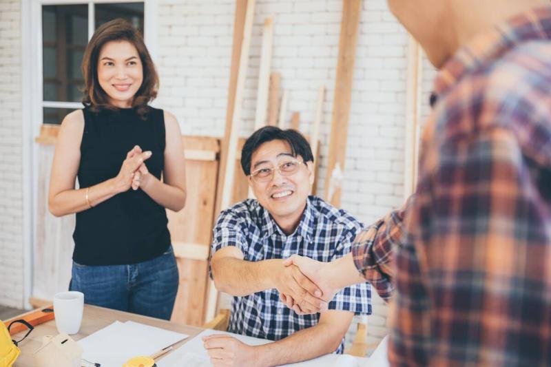 Contractor shaking hands with a man, while a woman stands nearby watching the scene