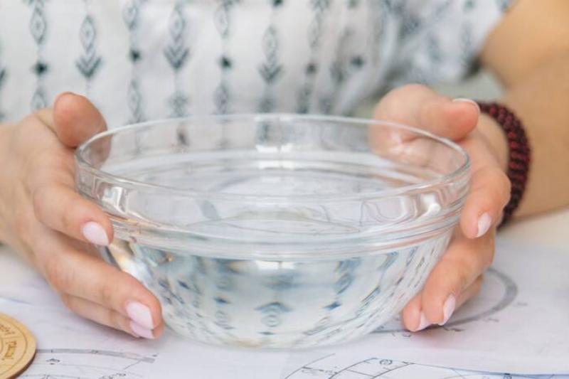 Woman off-screen sitting at a table with her hands wrapped around a glass bowl filled with water