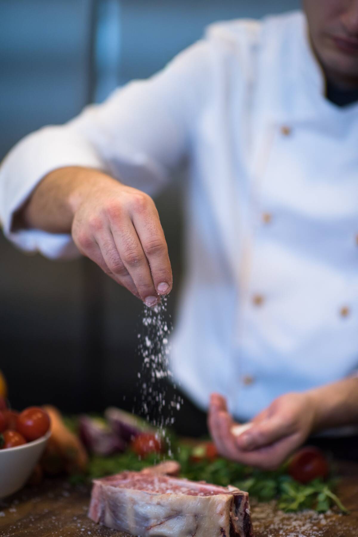 Chef seasoning a raw steak with salt