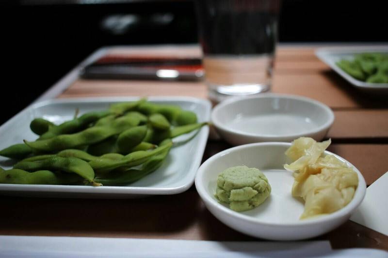 Plates of edamame and various condiments placed on a wooden table