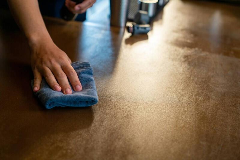 Person off-screen wiping down a wooden table with a blue cloth