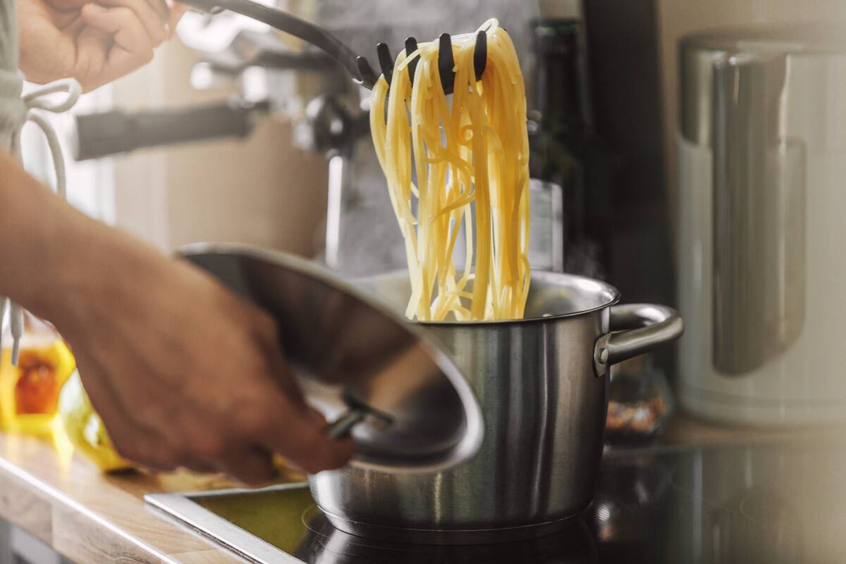 Person off-camera scooping up cooked pasta from a metal pot