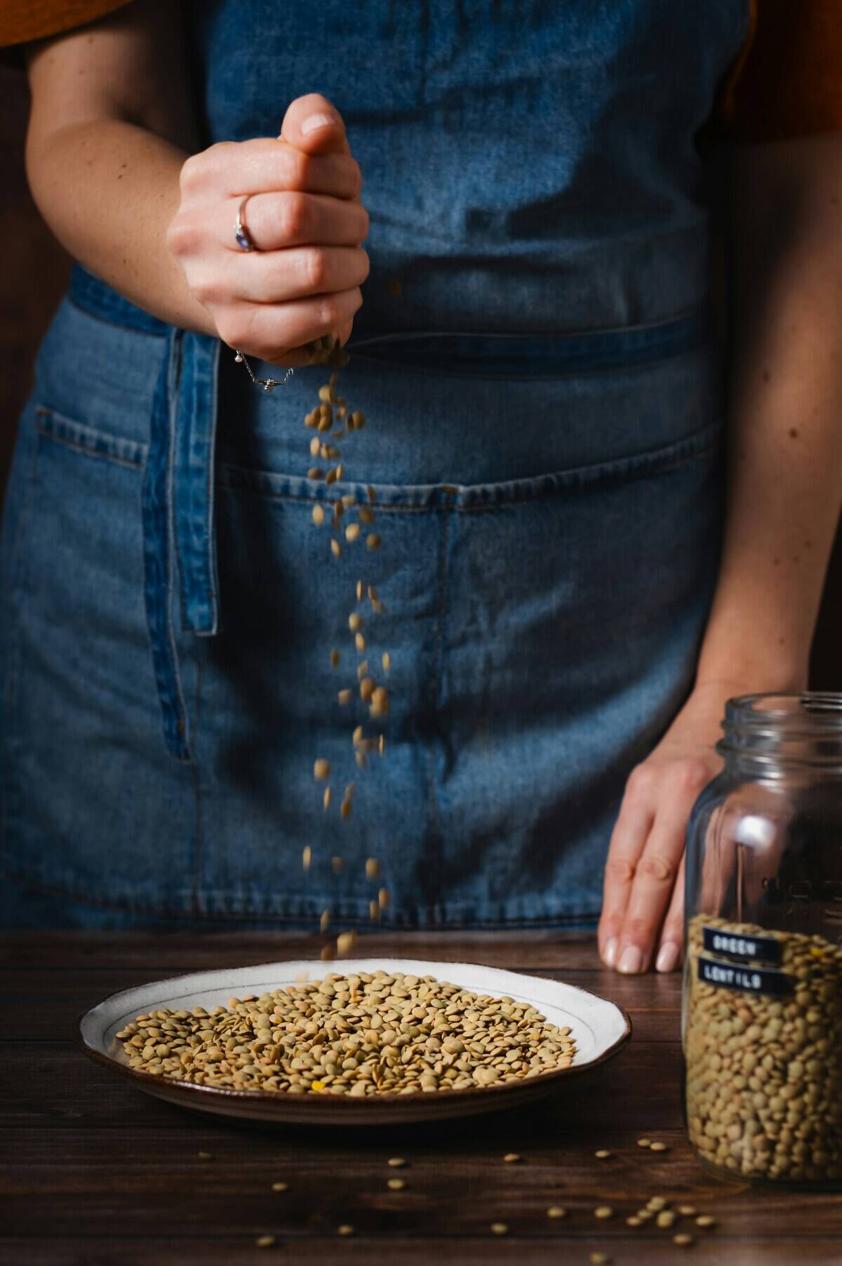 Woman letting lentils fall onto a plate from her hand. A jar filled with lentils is placed beside the plate