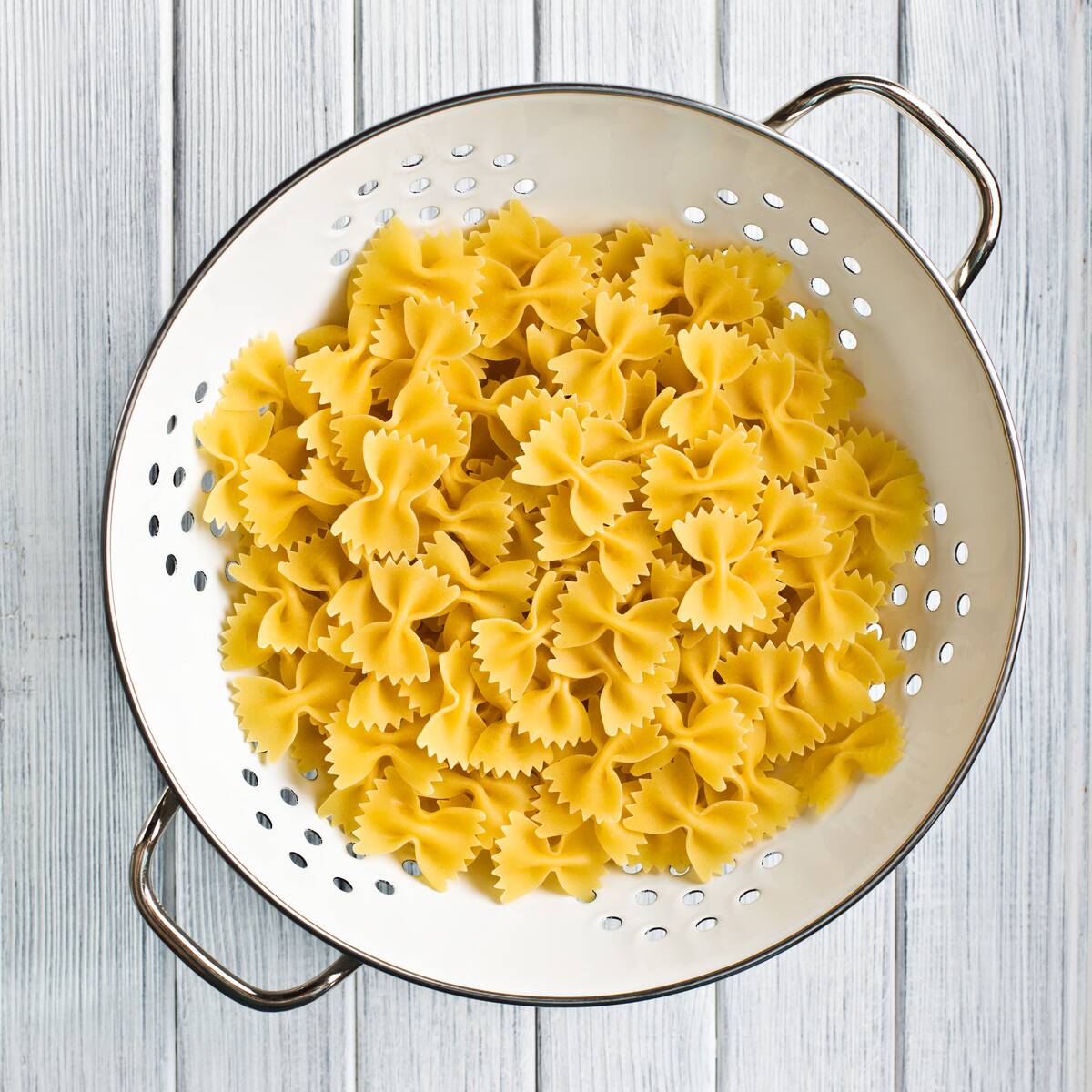 Pasta in a strainer that's been placed on a white wooden table