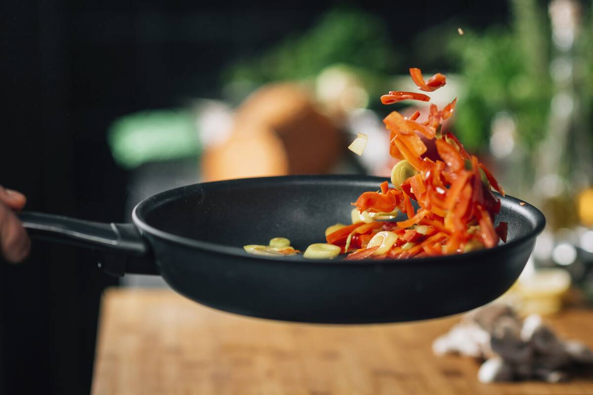Person off-screen flipping vegetables in a frying pan