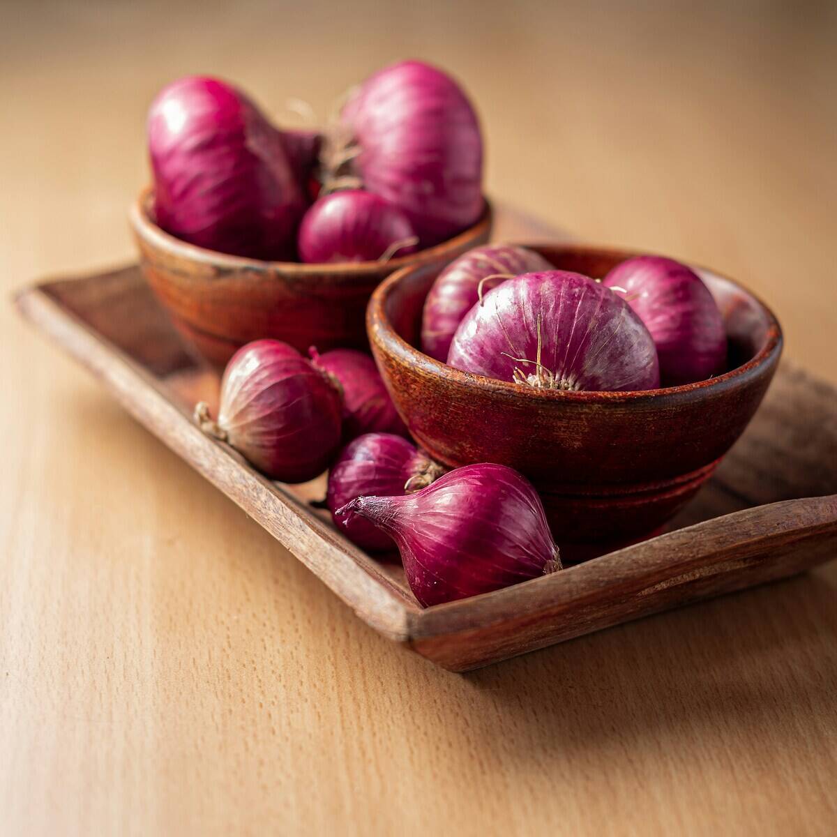 Whole red onions in wooden bowls and on a wooden tray