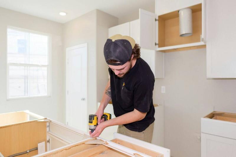 Man using a drill on a piece of wood at the edge of a kitchen counter