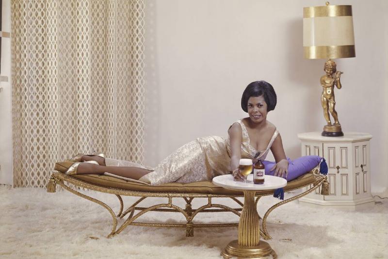 Young woman lying on sofa holding beer glass, smiling, portrait