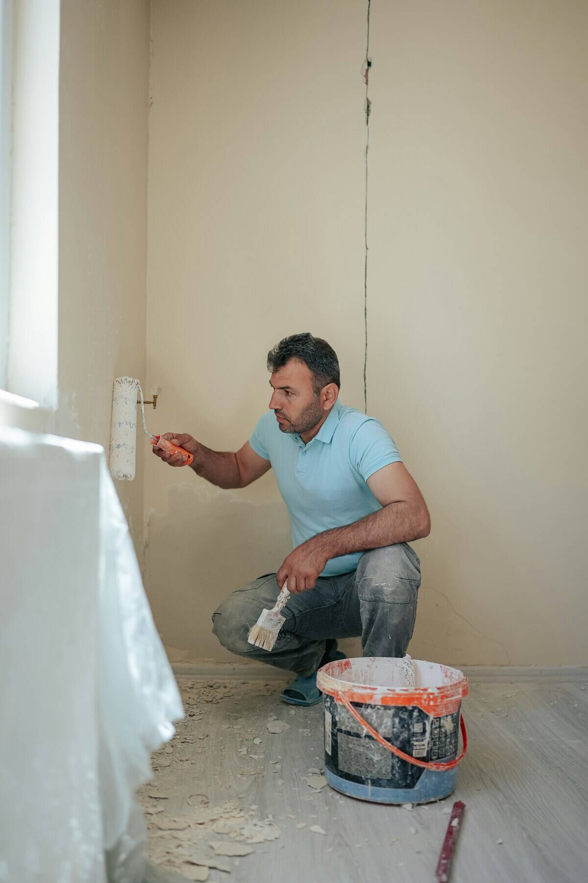 Man crouched in front of a wall, using a roller to apply paint