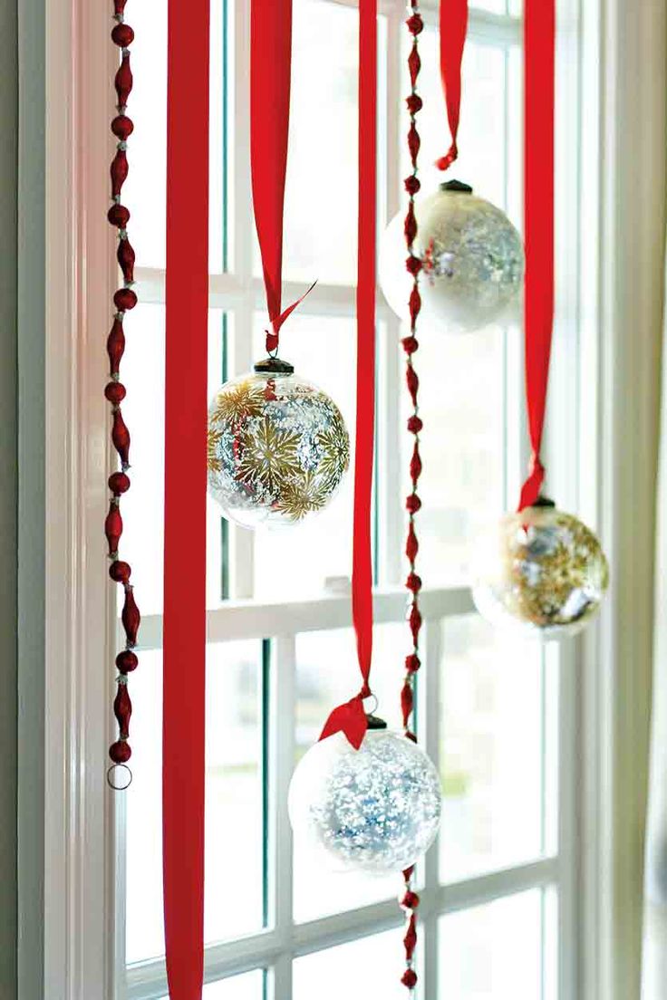 Silver and gold glass ball ornaments hung from red ribbon in a window
