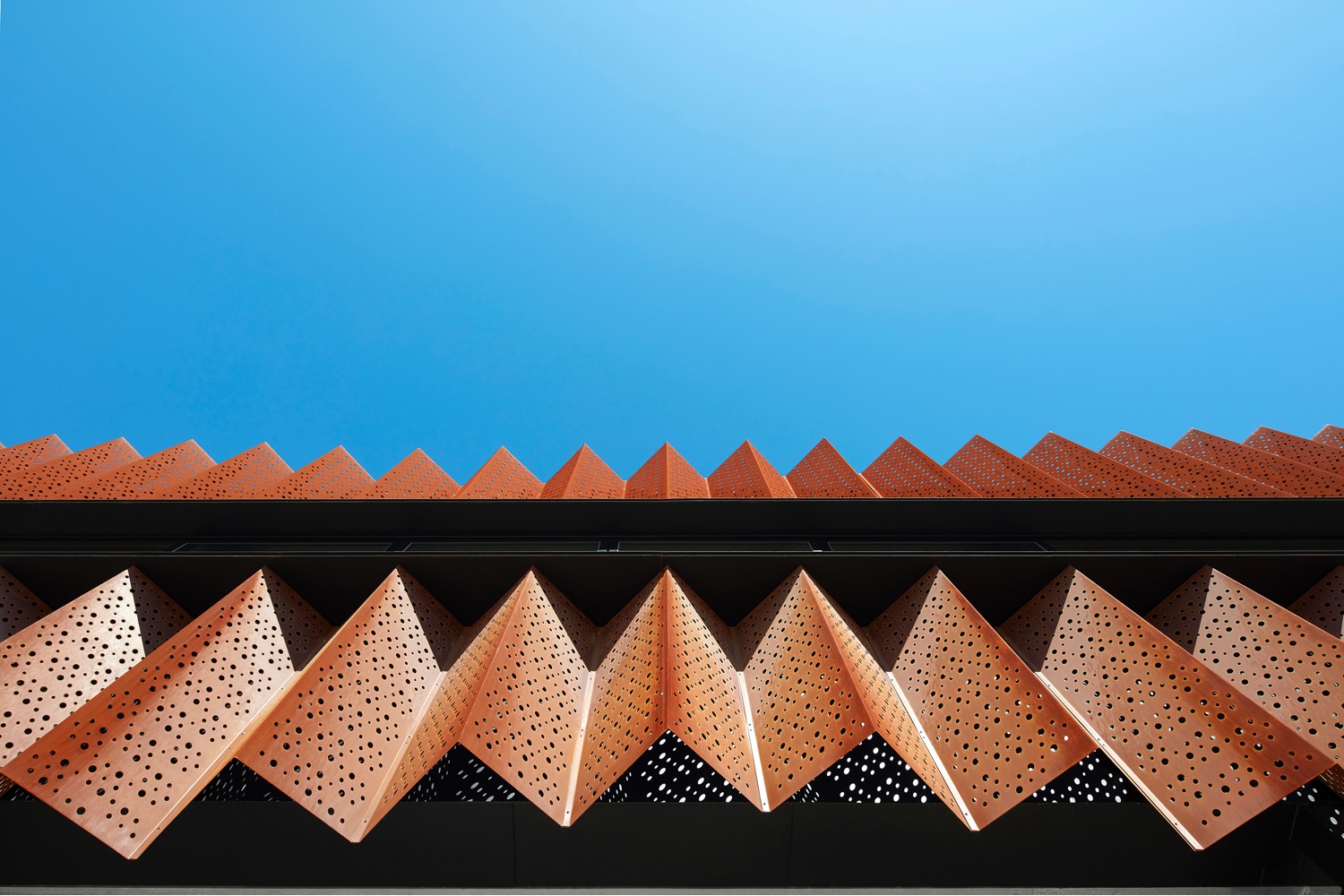The Flyover Gallery's black painted cement sheeting is clad with zig-zagging perforated cortex steel sheeting.
