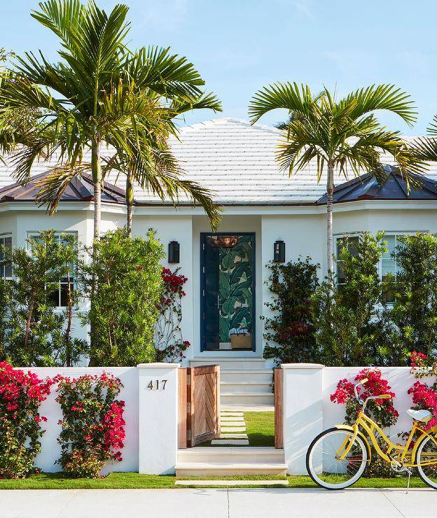 Brass door numbers are mounted beside a low wooden chevron gate opening to concrete pavers leading to stairs ending at a blue chevron front door.