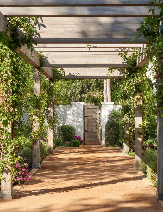 An ivy wrapped pergola leads to a brown wooden door.