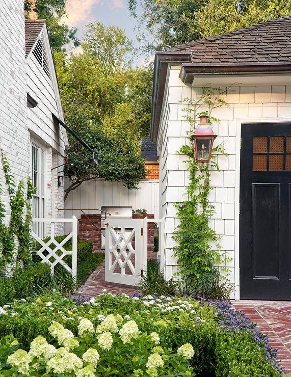 Red brick herringbone pavers lead past a beautiful garden to a white chippendale gate.